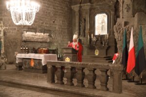 Ołtarz główny. Metropolita krakowski stoi przy solnej ambonie. W lewej dłoni dzierży pastorał. Ubrany jest w czerwony ornat