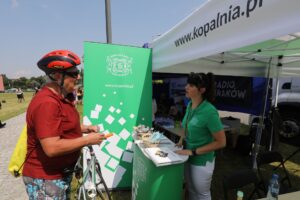 Promocyjne stoisko wielickiego uzdrowiska. Starszy pan w czerwonym rowerowym kasku rozmawia z pracownicą uzdrowiska