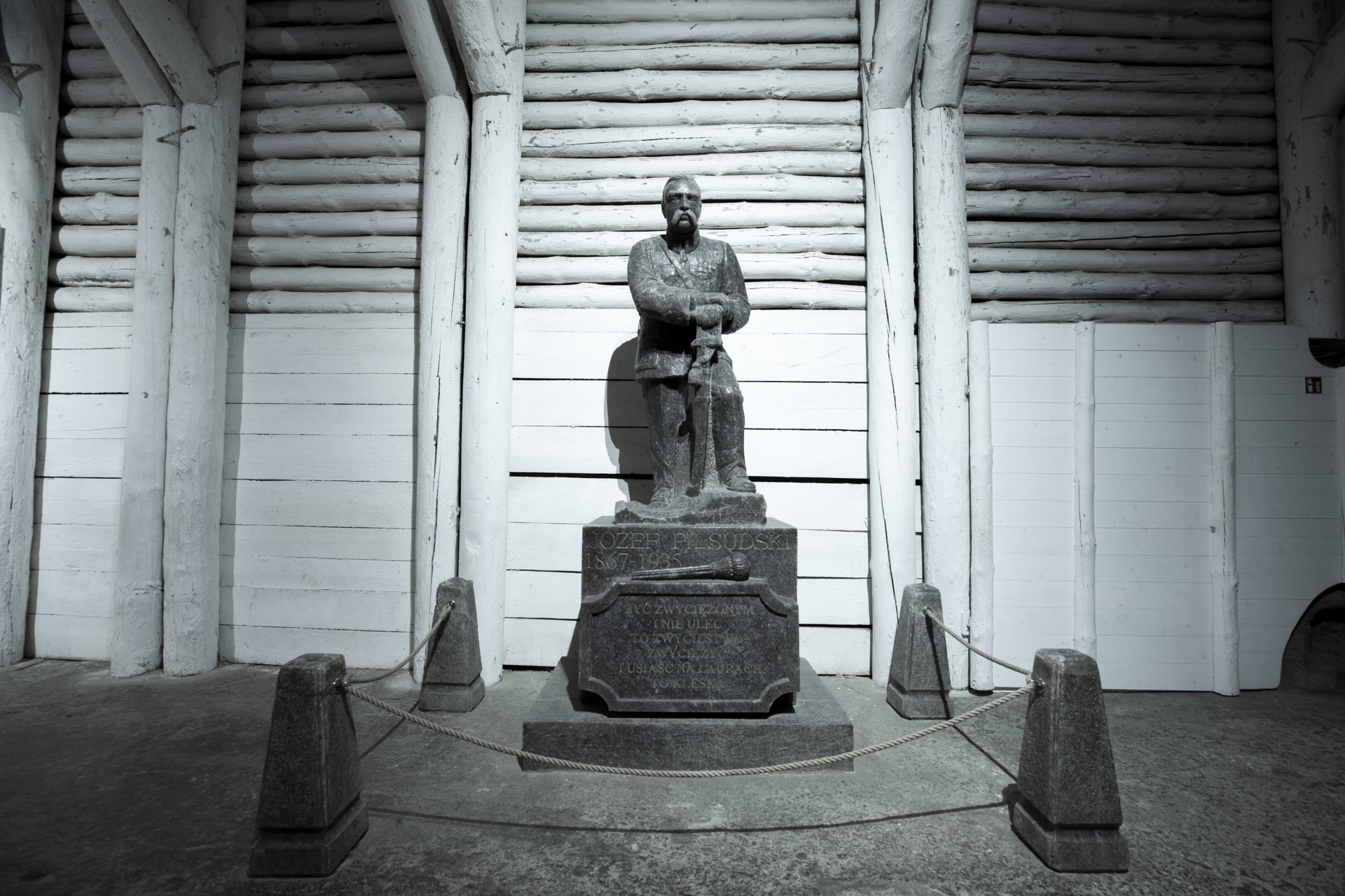 Solny pomnik Józefa Piłsudskiego. Marszałek stoi oparty o szablę na postumencie, w tle biała drewniana obudowa górnicza
