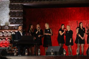 Występ Michała Matuszewskiego. Wokalista akompaniuje sobie na keyboardzie, w tle towarzyszące artyście kobiecie chórki - sześć wokalistek w czarnych sukienkach