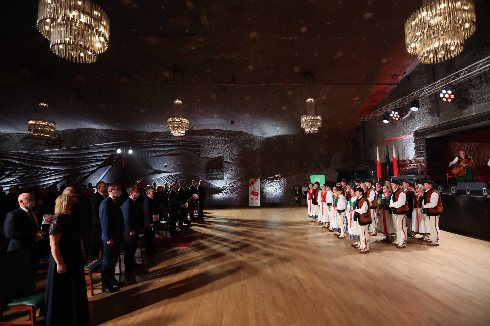 Góralski zespół śpiewa dla stojącej publiczności. Ponad głowami zebranych w komorze Warszawa szklane żyrandole