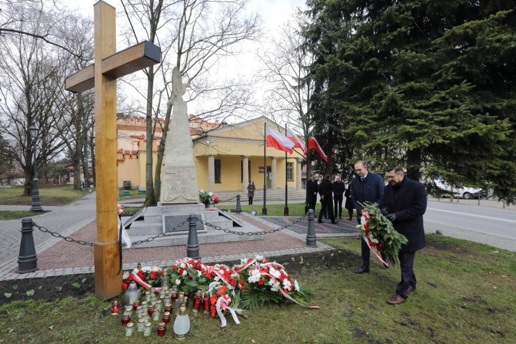 Krzyż katyński na wielickich Plantach. Kwiaty składają Prezes Paweł Nowak oraz Członek Zarządu Jan Ziobro. W tle budynek wielickiego magistratu