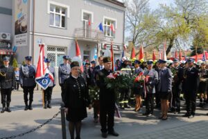 Białe czerwone kwiaty od związków zawodowych. W tle stoją policjanci i strażacy