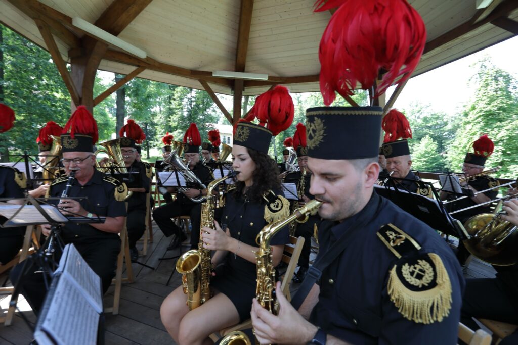 Koncert orkiestry w parkowej altanie. Na pierwszym planie młody saksofonista