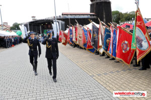 Uroczysty apel na tle tężni Kopalni Soli "Wieliczka". Komendant straży przechodzi z salutem wzdłuż szpaleru sztandarów