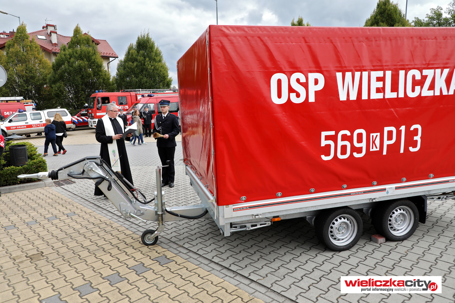 Poświęcenie strażackiej przyczepy. Na czerwonej plandece napis OSP Wieliczka
