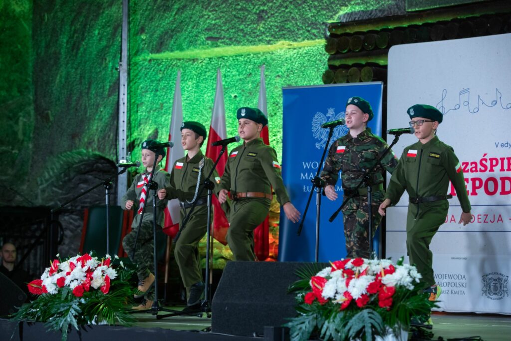 Pięciu chłopców w żołnierskich mundurach. Śpiewają i maszerują w miejscu