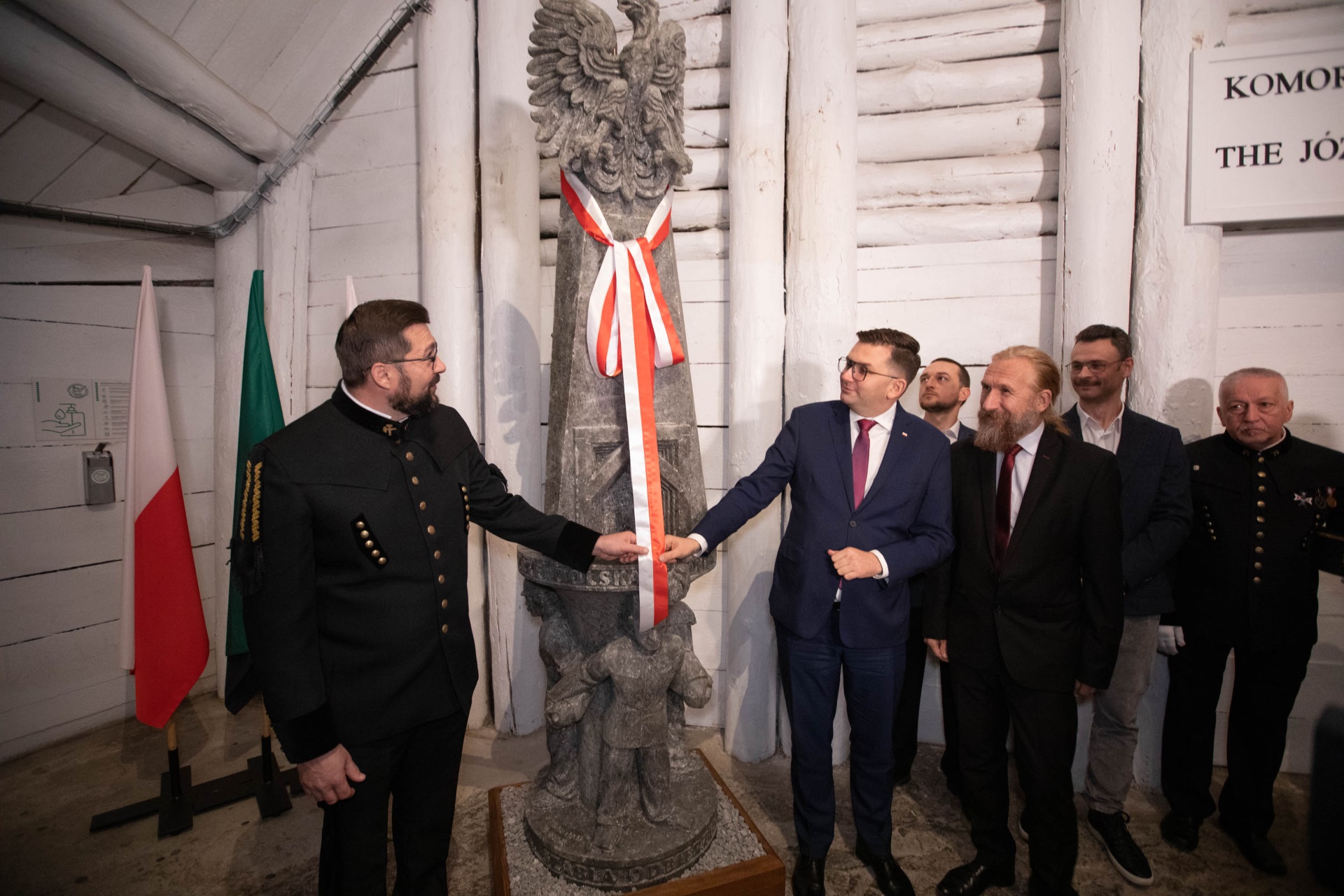 Prezes Paweł Nowka i Wojewoda Łukasz Kmita zdejmują z rzeźby biało-czerwoną szarfę