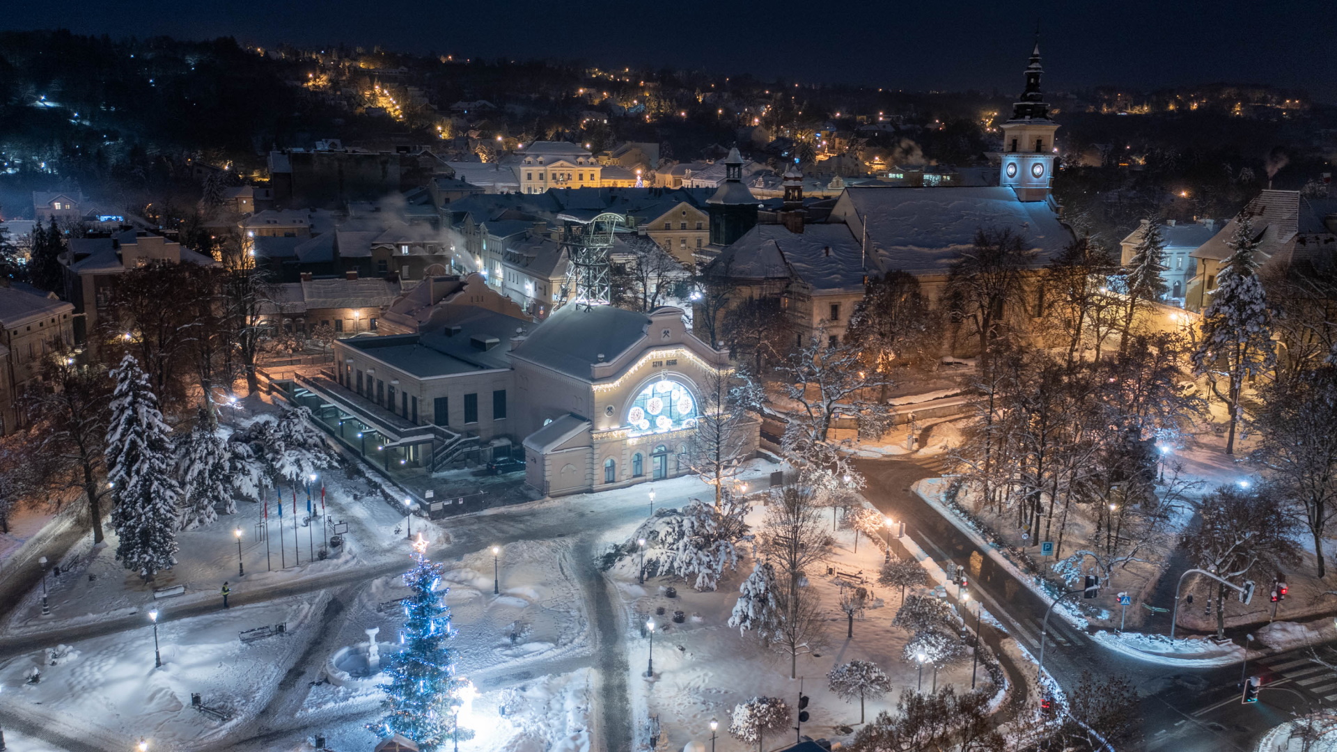 Widok z lotu ptaka na zimową Wieliczkę. Ośnieżone nadszybie szybu Regis, wokół świąteczne iluminacje. Zdjęcie zrobione przed wschodem słońca