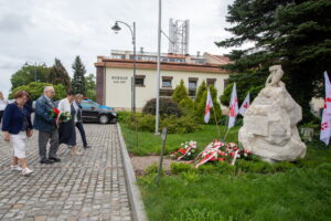 Delegacja składa kwiaty. W tle zatknięte na jeżu białe flagi z napisem "Solidarność"