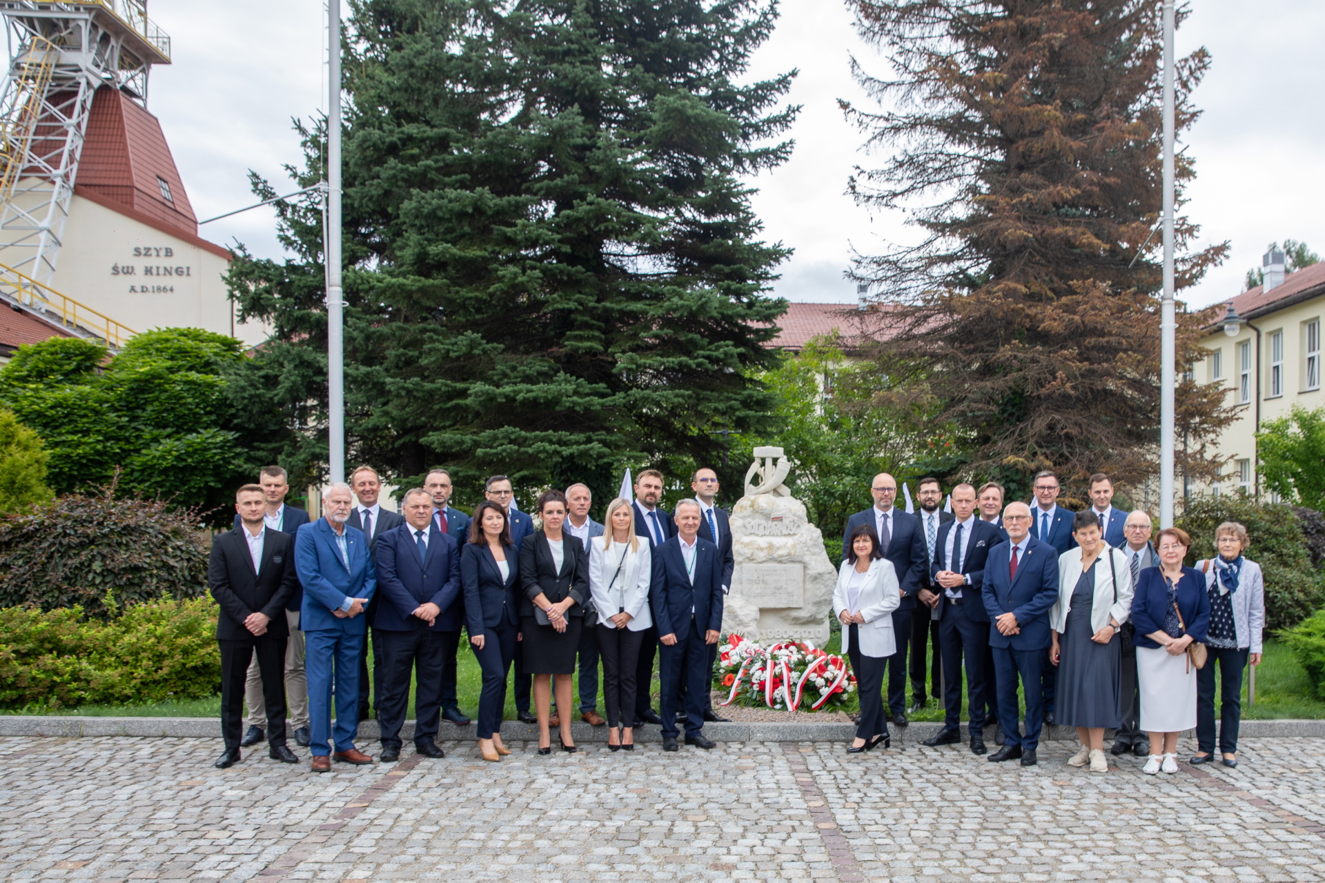 Uczestnicy uroczystości. Pamiątkowe zdjęcie na tle pomnika, w głębi nadszybie oraz wieża szybowa szybu św. Kingi