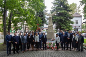 Zdjęcie grupowe. W tle pomnik zwieńczony orłem z rozpostartymi skrzydłami