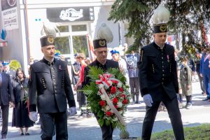 Trzech górników w galowych mundurach podchodzi do pomnika z wieńcem biało-czerwonych kwiatów