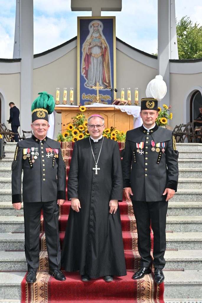 Biskup Robert Chrząszcz, Prezes Marian Leśny i Członek Zarządu Łukasz Sadkiewicz. W tle stopnie ołtarza oraz obraz przedstawiający św. Kingę