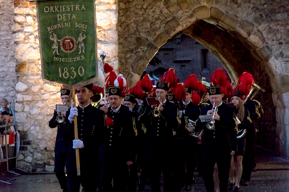 Górnicza orkiestra przechodzi przez Bramę Floriańską. Na pierwszym planie zielony proporzec orkiestry