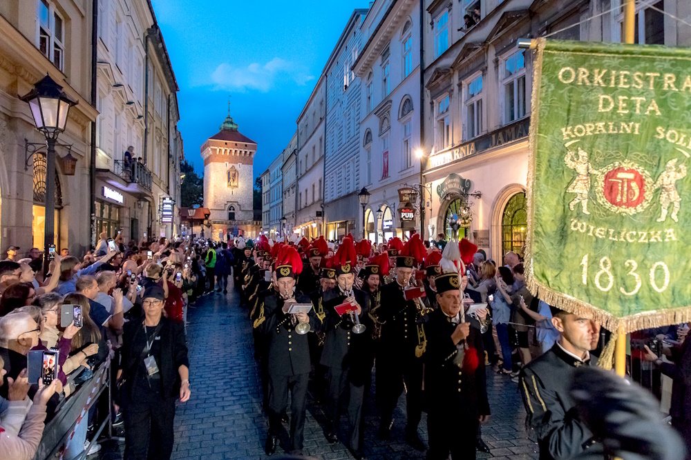 Orkiestra górnicza maszeruje ulicą Floriańską. W kadrze proporzec orkiestry z datą 1830