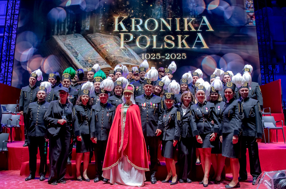 Górnicza delegacja. Pamiątkowe zdjęcie na scenie. W tle na telebimie obraz i hasło: Kronika Polska 1025-2025