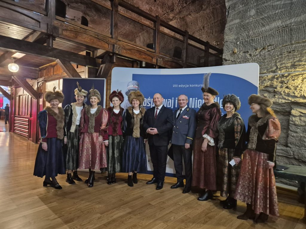 Pamiątkowe zdjęcie na tle ścianki z napisem "Zaśpiewaj i Ty Niepodległej"