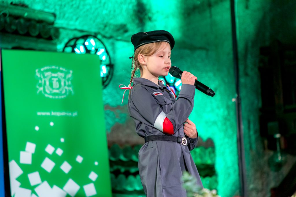 Laureatka podczas występu. Dziewczynka w harcerskim mundurze, w czarnym berecie