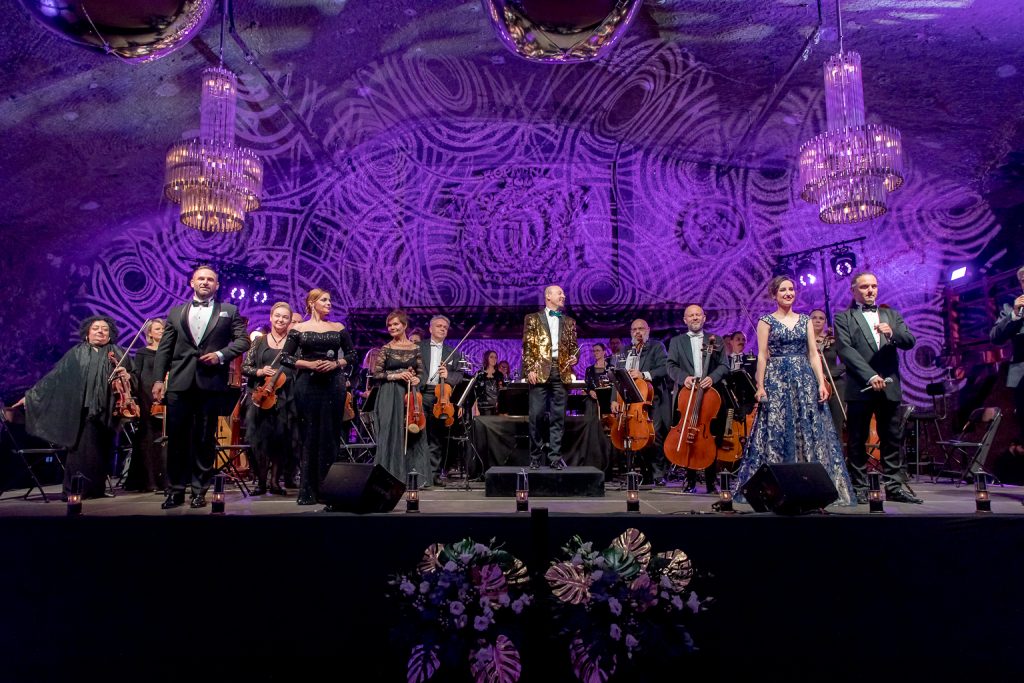 Soliści na scenie, orkiestra. Fioletowa iluminacja komory