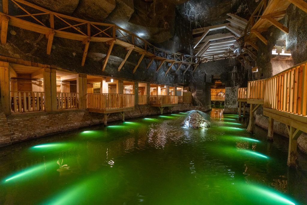 Komora Wessel. Widok na solankowe jezioro. Tafla wody w kolorze zielonym, podświetlona, po bokach galeryjki z jasnego drewna