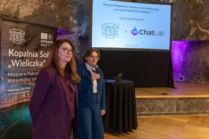 Prezes Barbara Zięba-Godula i rzecznik prasowy Agnieszka Wolańska otwierają spotkanie. W tle ekran z prezentacją. Panie stoją po lewej stronie kadru