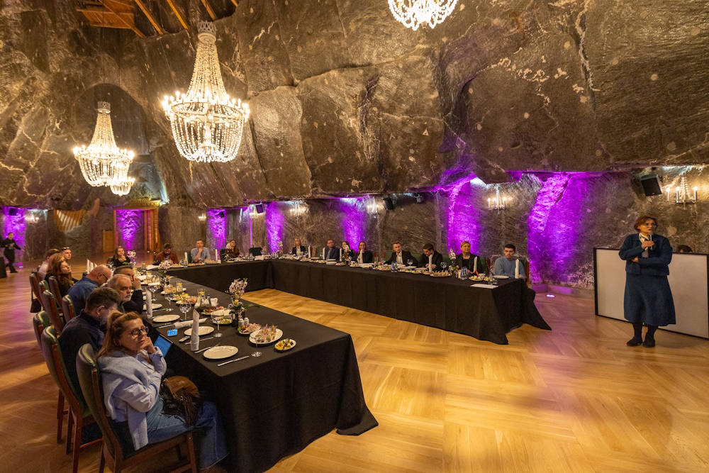 Uczestnicy spotkania siedzący za stołem. W tle solne ociosy, czyli ściany oraz żyrandole