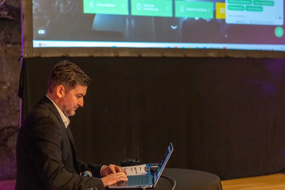 Paweł Rusecki. Siedzi przed laptopem, na którym prezentuje zebranym możliwości sztucznej inteligencji