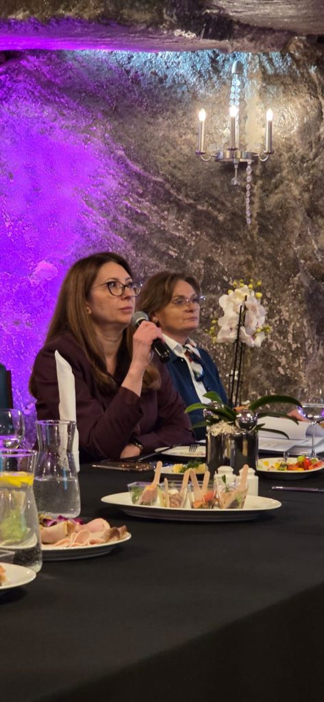 Prezes Barbara Zięba-Godula odpowiada na pytanie dziennikarza. W tle podświetlona na fioletowo solna ściana. Obok pani prezes siedzi Agnieszka Wolańska, rzecznik prasowy kopalni