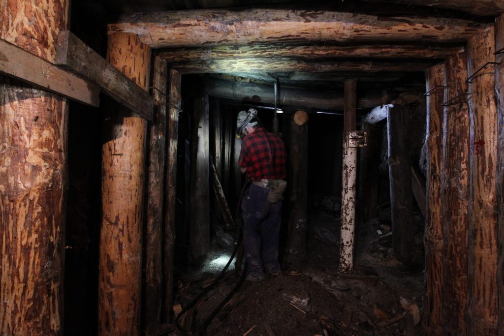 Górnik pracujący w głębi chodnika obudowanego drewnem