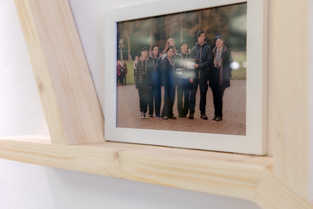 Zdjęcie harcerzy w białej ramce, stoi na półce z jasnego sosnowego drewna