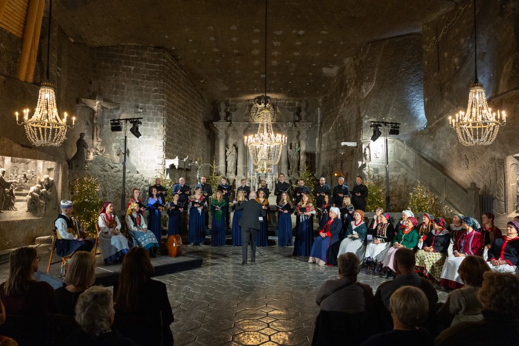 Artyści na tle ołtarza w kaplicy św. Kingi, Po prawej stronie kadru siedzą panie w strojach regionalnych