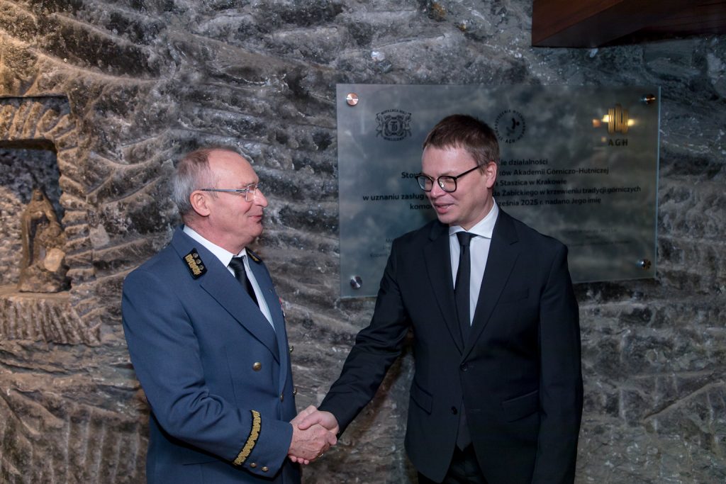 Prezes kopalni i prezes Wisły Kraków podają sobie ręce. W tle szara solna ściana