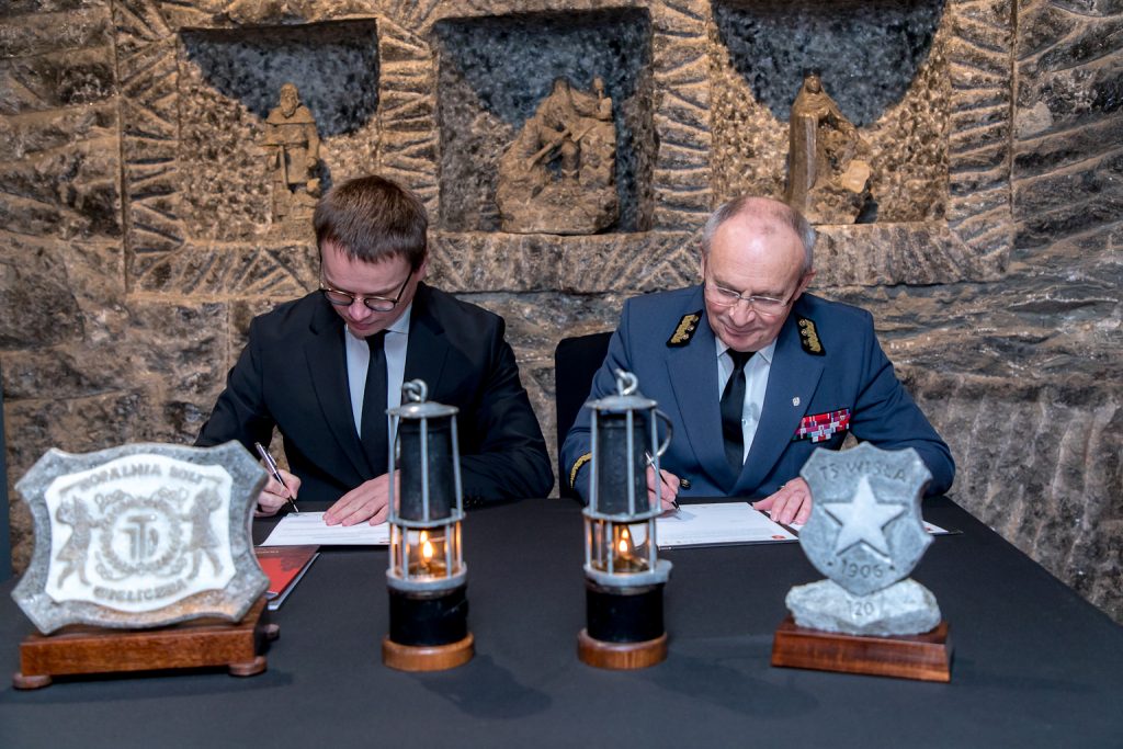 Prezesi składają podpisy na dokumencie. Siedzą przy nakrytym na czarno stole