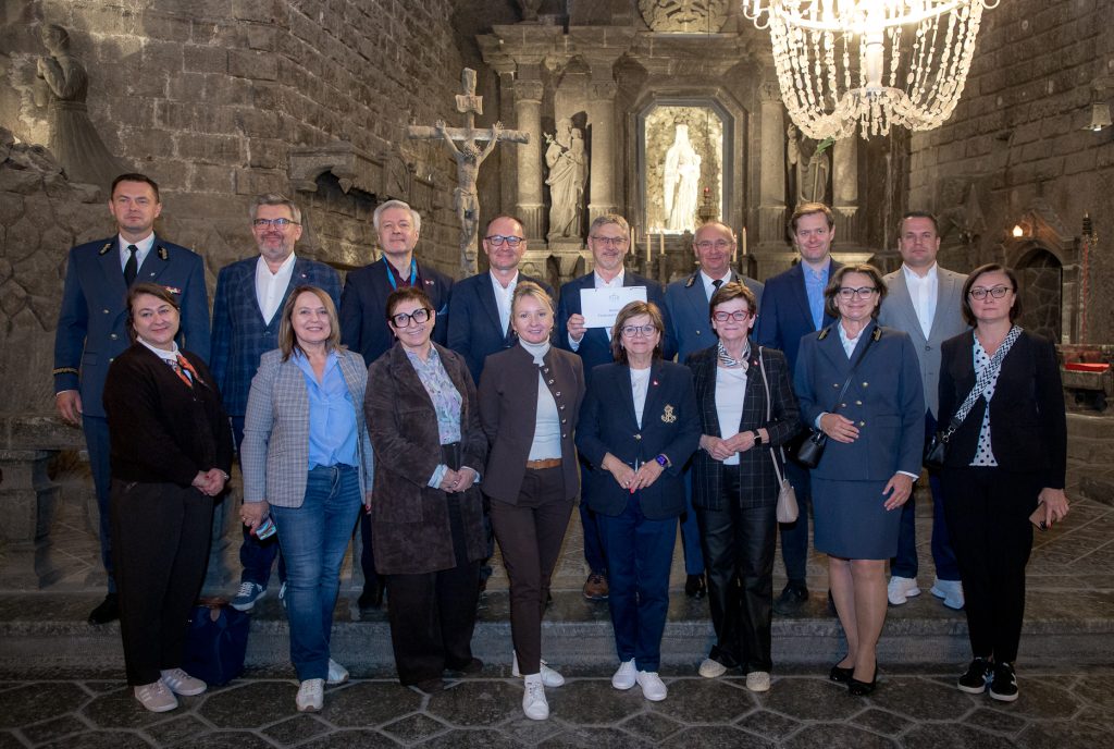 Grupowe zdjęcie członków komisji na tle ołtarza głównego w kaplicy św. Kingi. W głębi widoczna solna figura św. Kingi, podświetlona