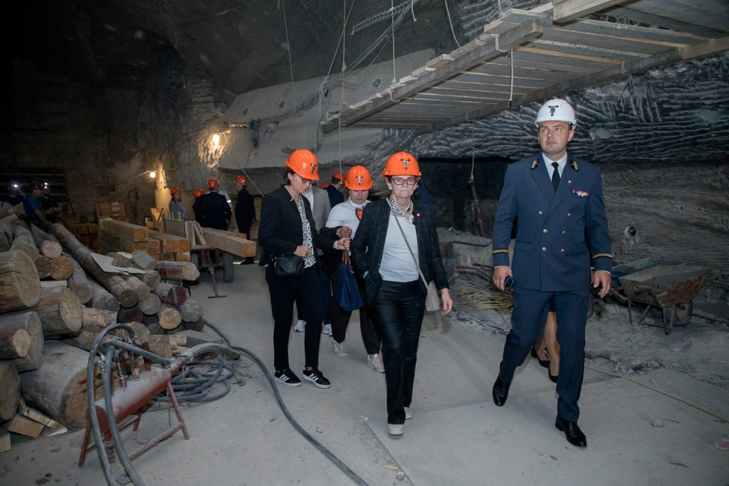 Wiceprezes Sadkiewicz, w białym hełmie, oprowadza członków komisji (państwo w kaskach czerwonych) po remontowanej komorze Warszawa