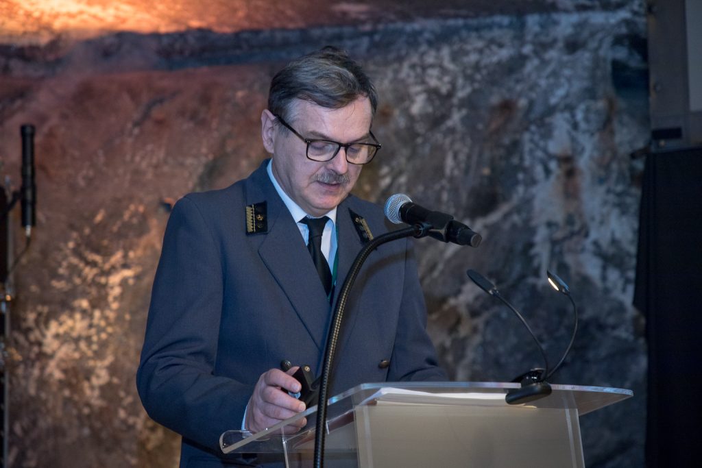 Przedstawiciel kopalni Jarosław Chwałek w szarym codziennym mundurze. Wypowiedź przy mównicy. Zbliżenie